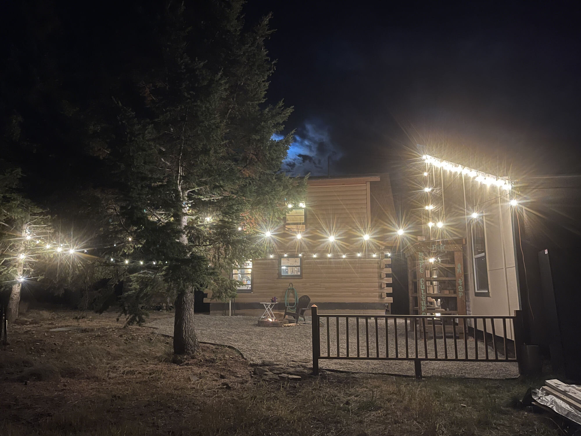 The cabin and fire pit under party lights strung between the trees