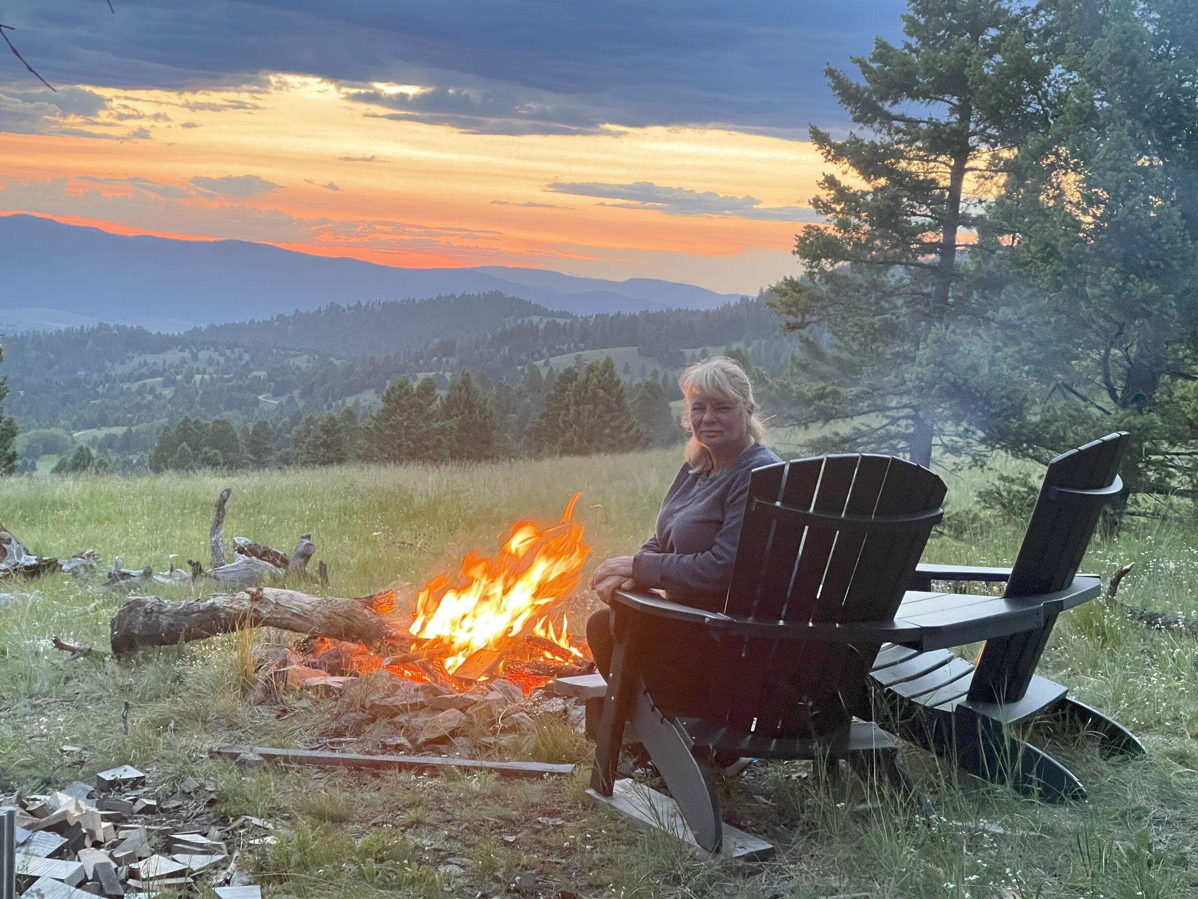 Two Adirondack chairs at the fire pit, a person settled in, the sun setting behind the ranges