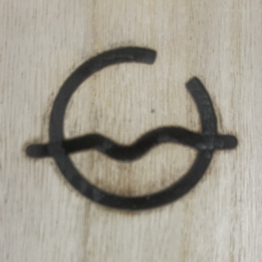 The Sweetwater Ranch brand burned into wood — a water-wave flowing through an open circle