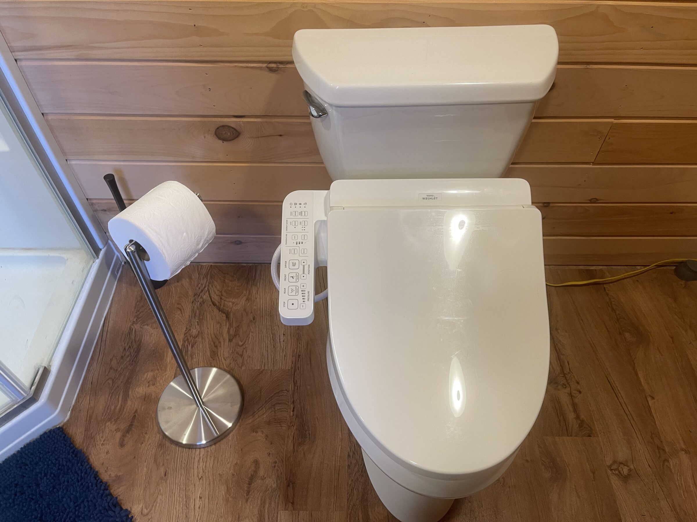 The Main Cabin bathroom at Sweetwater Ranch — a Toto Washlet bidet beside a glass corner shower, finished in warm knotty pine