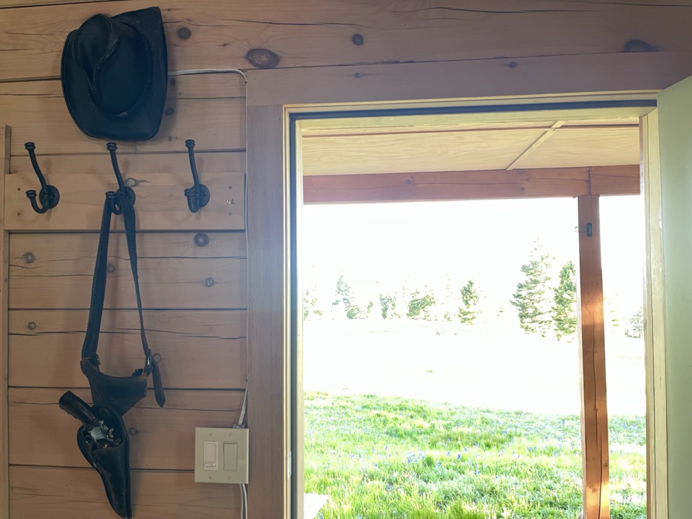 A cowboy hat and holstered revolver hanging by a cabin window framing the meadow at Sweetwater Ranch