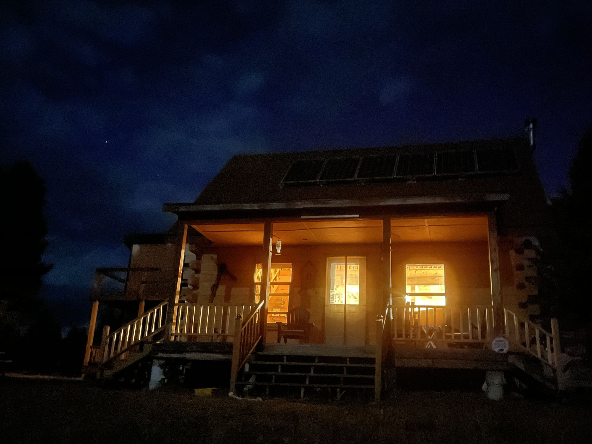 The log cabin at Sweetwater Ranch lit warm at night, running on its own solar power under a Montana sky