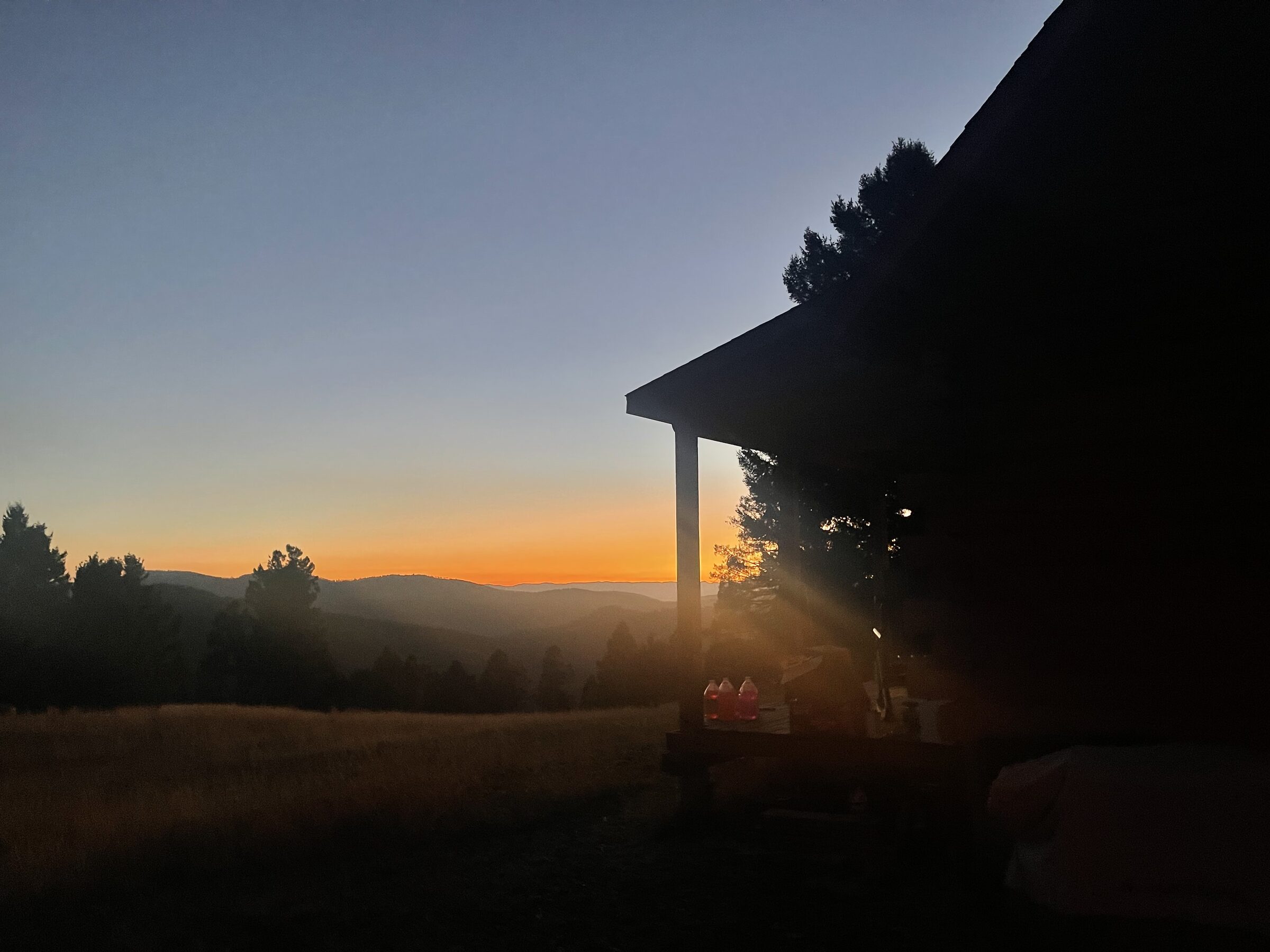 The Main Cabin at Sweetwater Ranch in silhouette at dusk, the valley going to embers and the porch beyond