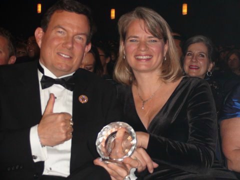 Terry L. Fossum in a tuxedo holding a small glass trophy, his wife Michelle beside him