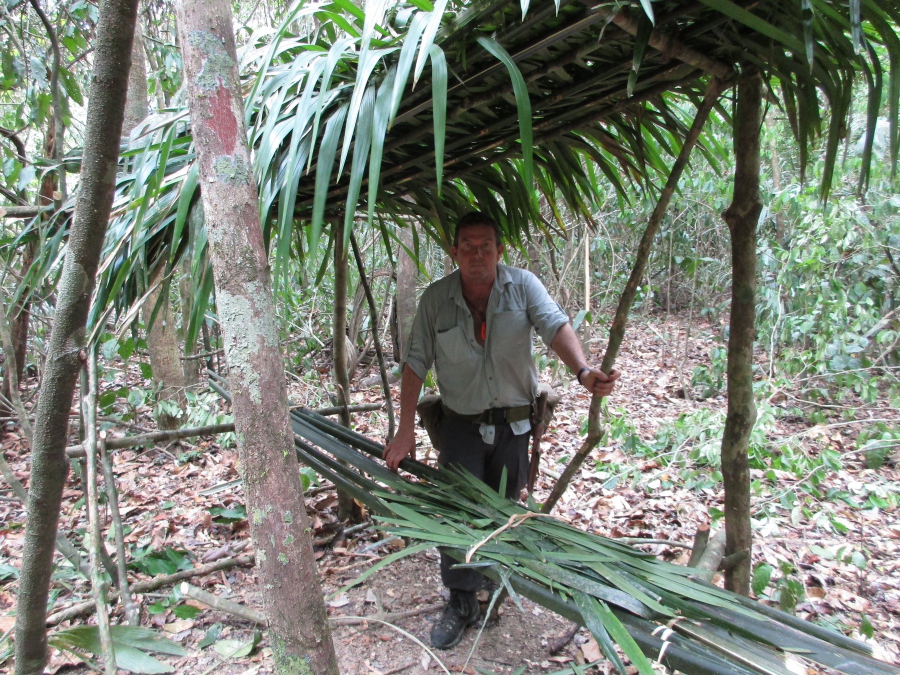 Terry L. Fossum beside the palm-thatched survival shelter he built in the jungle
