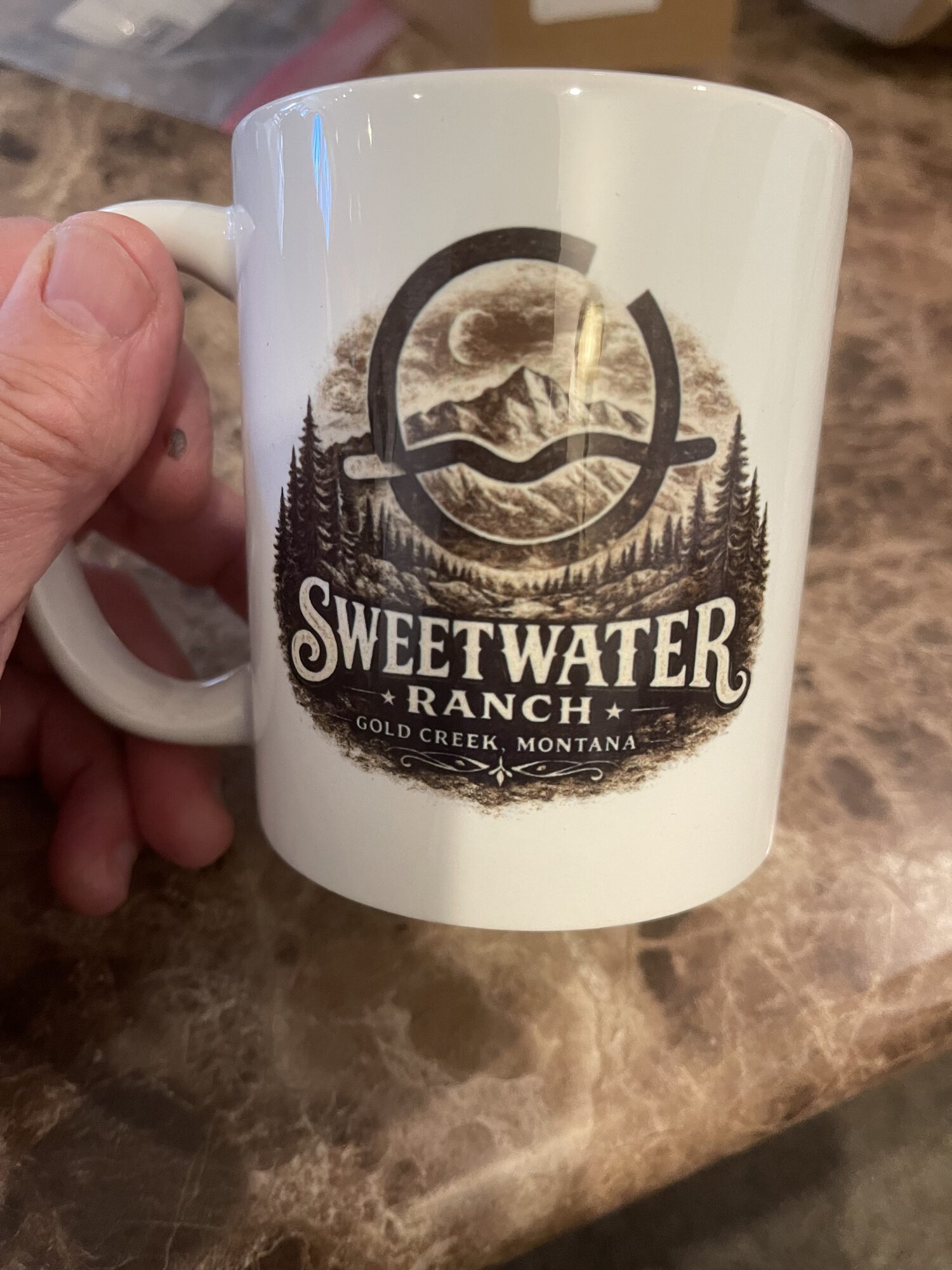 A Sweetwater Ranch mug carrying the ranch crest — the brand mark over a Montana mountain, Gold Creek, Montana