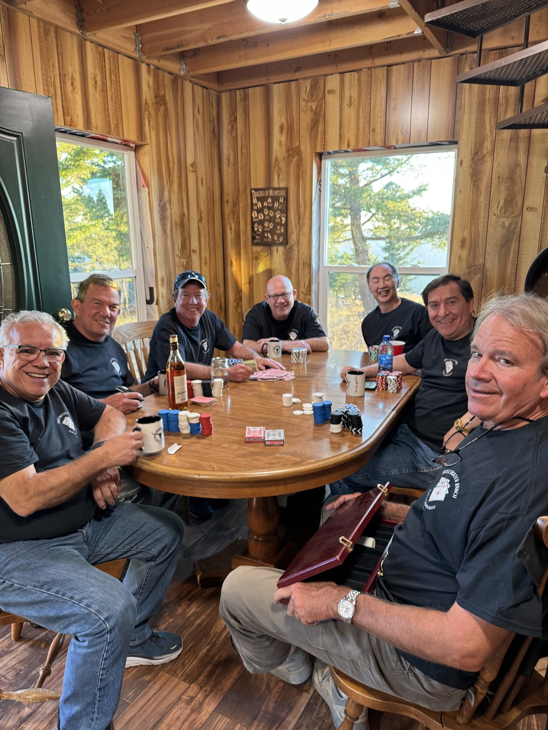 A group of friends in matching Sweetwater Ranch shirts around the cabin's poker table with chips and cards
