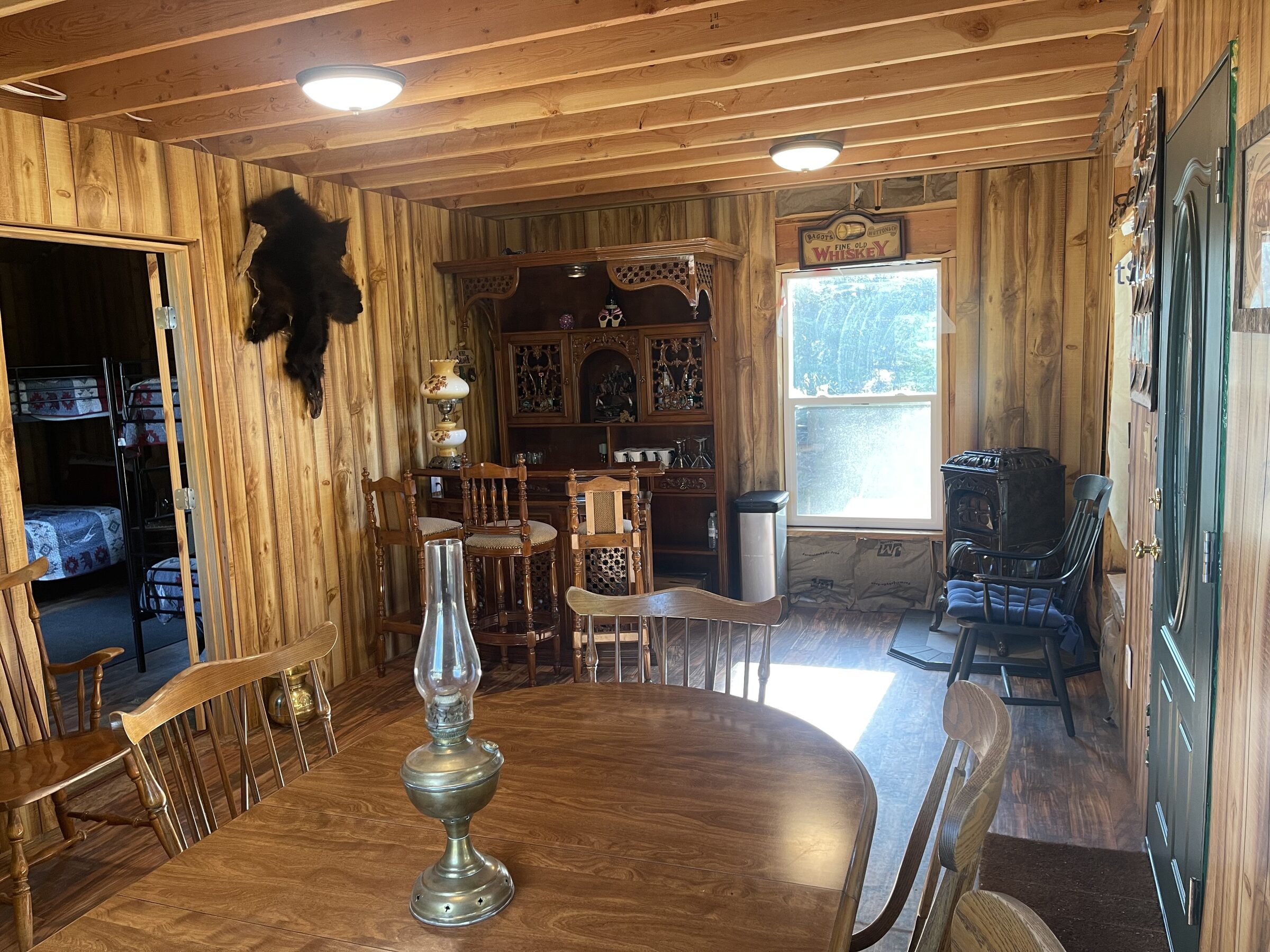 The interior of the Whiskey Ridge Saloon at Sweetwater Ranch — a long table, a bear hide on the knotty-pine wall, an ornately carved back-bar, a Fine Old Whiskey sign, an antique parlor stove, and the bunk room beyond