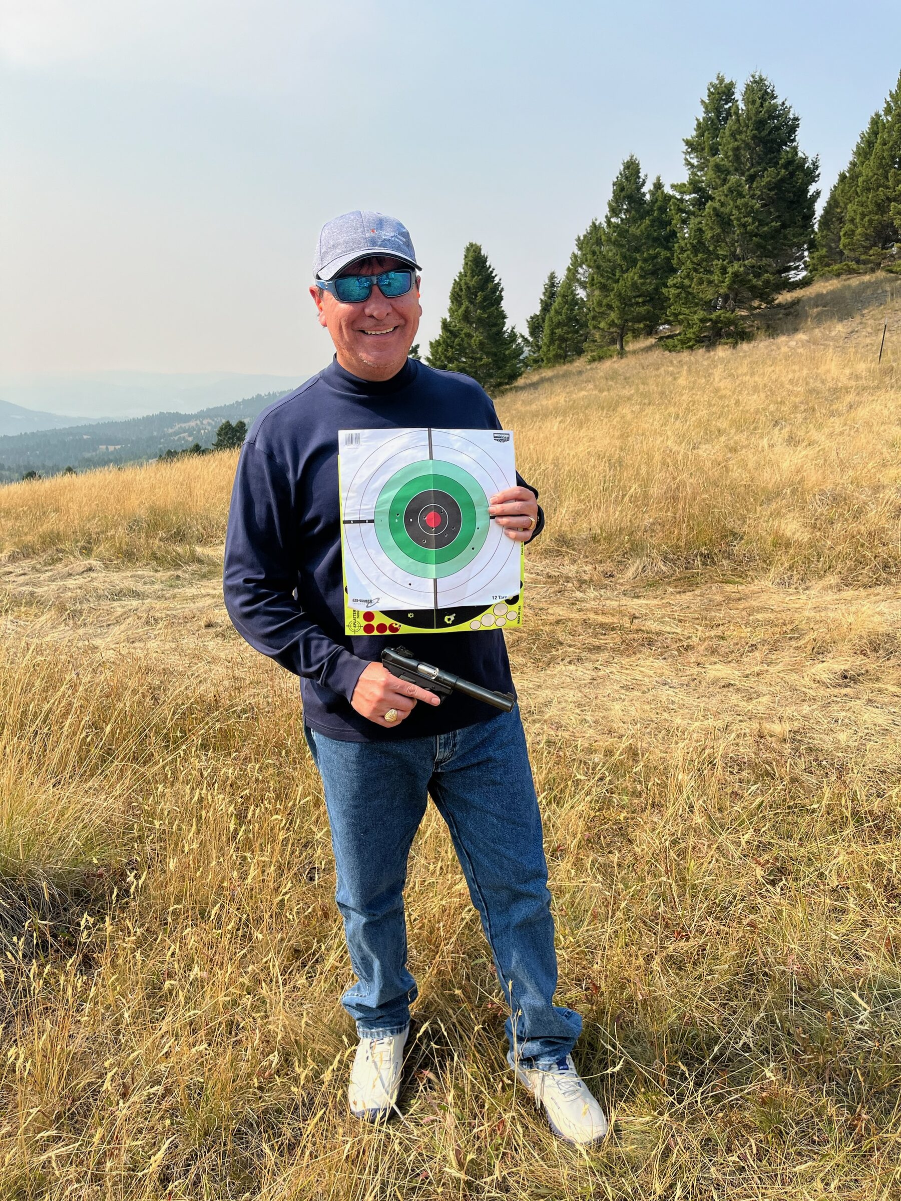 A tight target group held up beside a pistol on the private shooting range at Sweetwater Ranch, Montana mountains beyond