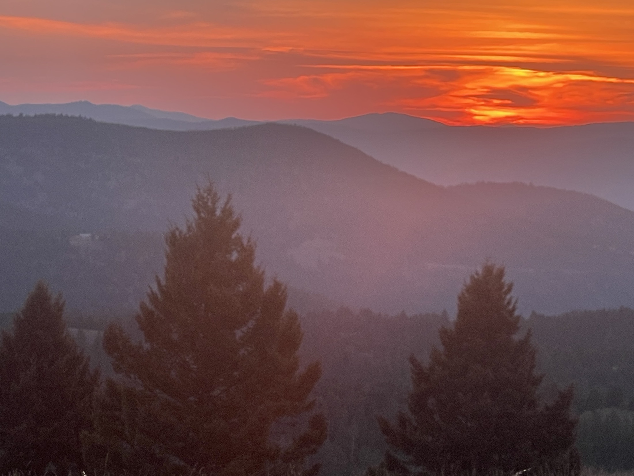 A fiery red and orange sunset over layered blue mountain ranges at Sweetwater Ranch, Montana