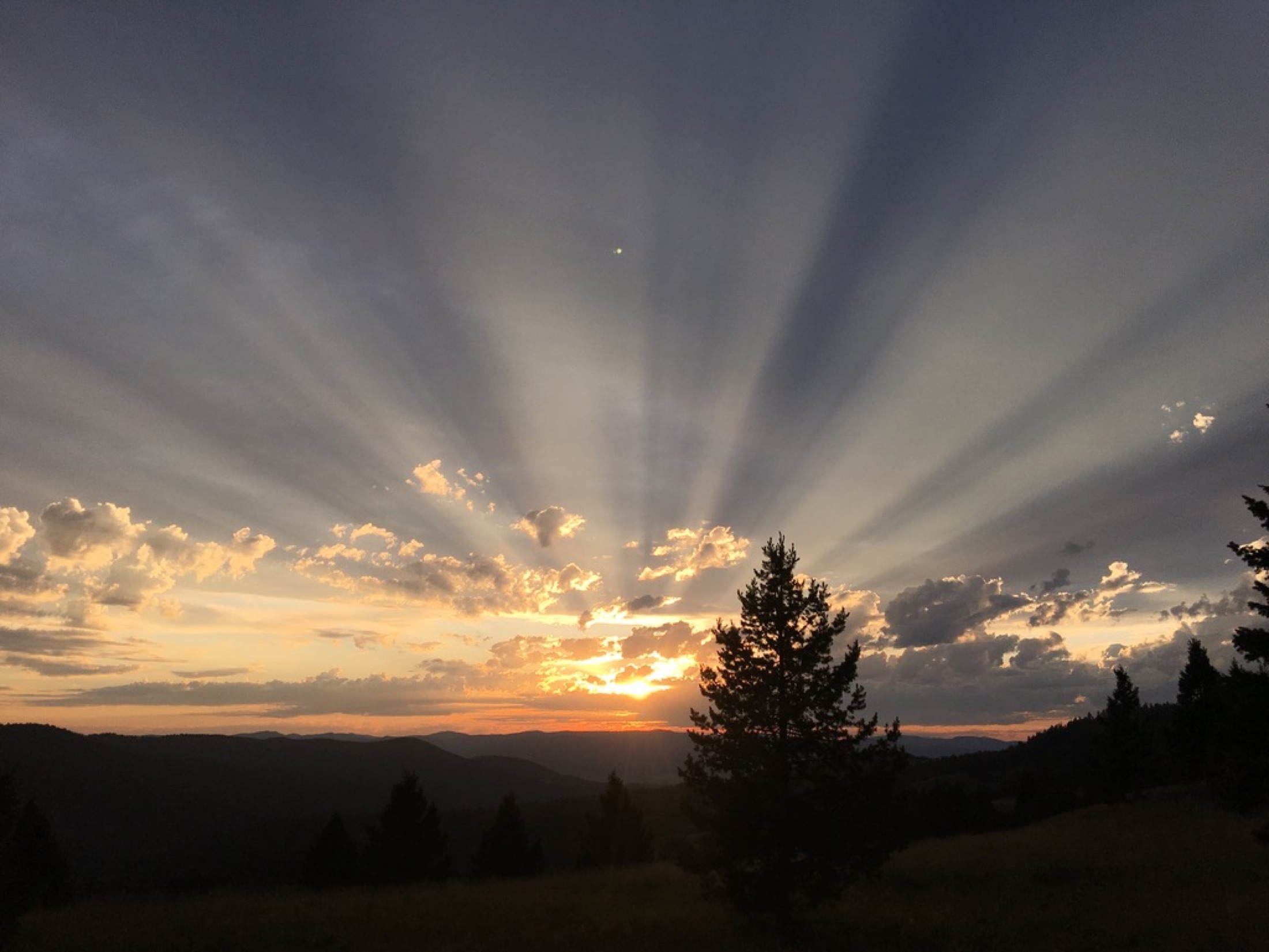 Dramatic crepuscular sun rays over the mountains at sunset, seen from Sweetwater Ranch, Montana
