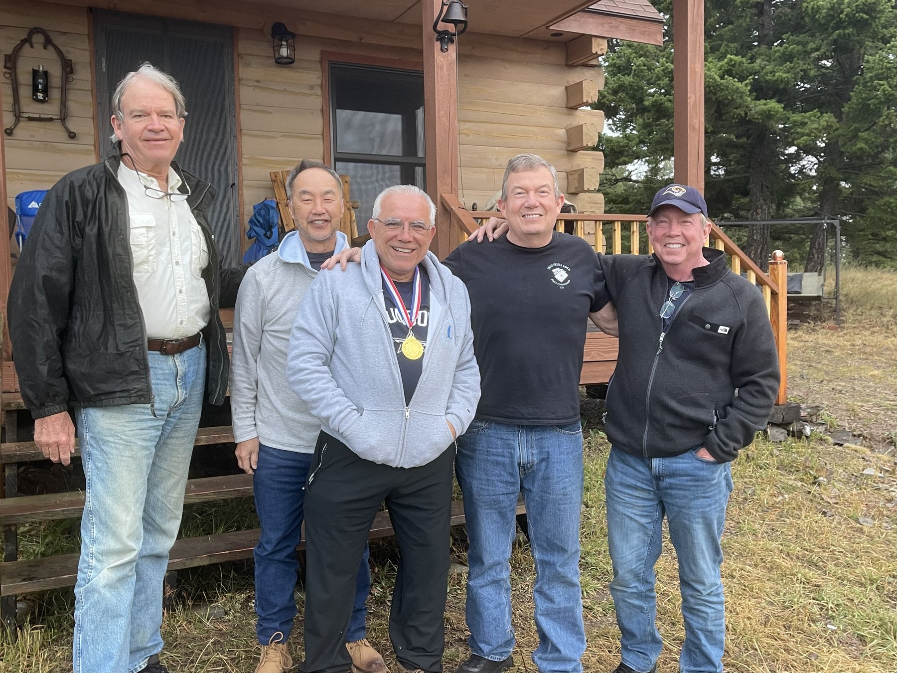 Five guests grinning in front of the log cabin at Sweetwater Ranch after a day of team-building games