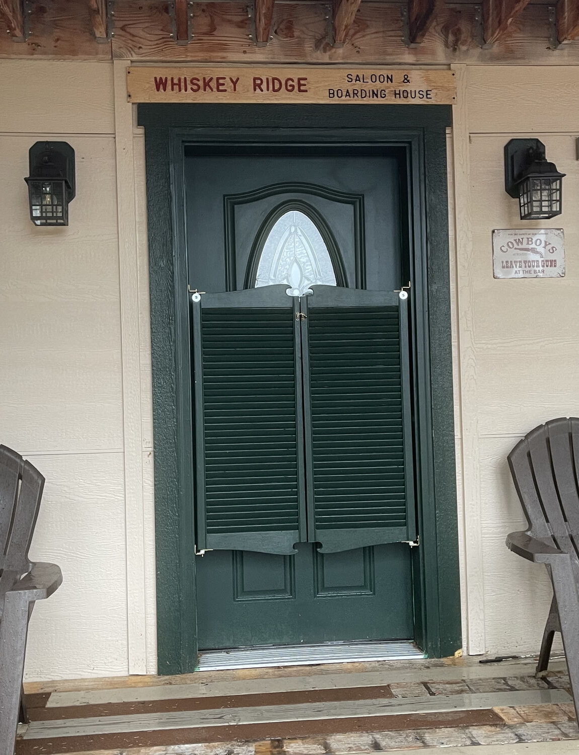 Green swinging saloon doors beneath the hand-painted Whiskey Ridge Saloon & Boarding House sign at Sweetwater Ranch
